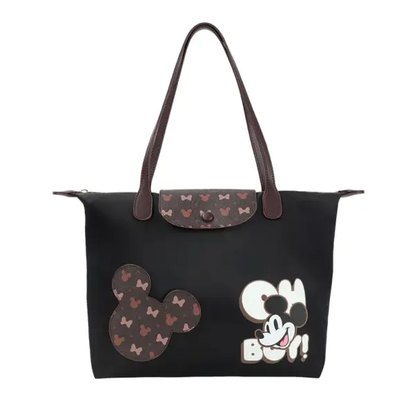 Front view of a black Disney-inspired tote bag with Mickey Mouse patch and monogram flap closure.