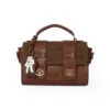 Front view of the brown MESUCA x Disney satchel bag featuring a cute white Mickey glove charm, gold buckles, and embossed logo.