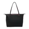 Back view of a plain black nylon tote bag with patterned snap button flap and brown leather handles.