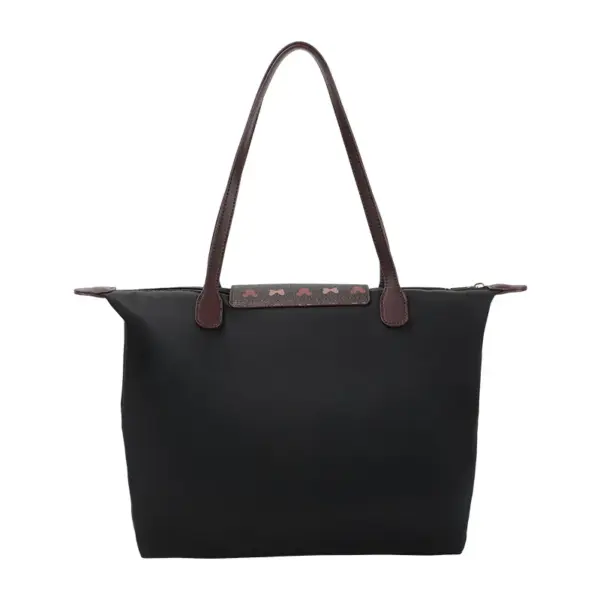 Back view of a plain black nylon tote bag with patterned snap button flap and brown leather handles.