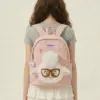 A young woman wearing a pastel pink padded school bag with a prominent 3D fluffy sheep face applique, big glasses, and zippered front pocket.