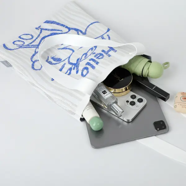 Flat lay showing a white woven tote bag holding a tablet, phone, umbrella, perfume, and makeup, demonstrating spacious interior.