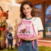 A smiling woman holding a pink Zootopia themed knit bucket bag with Nick and Judy design, outdoor theme park background.