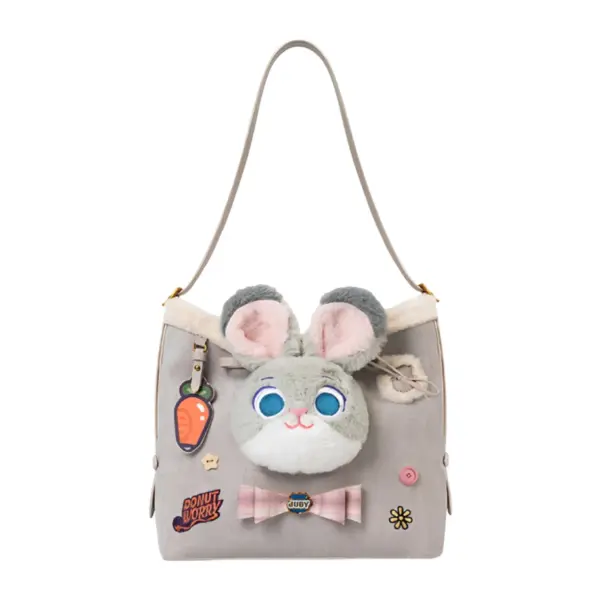 Front view of a light grey faux suede shoulder bag featuring a plush Judy Hopps bunny face, carrot charm, and "Donut Worry" embroidery patch.