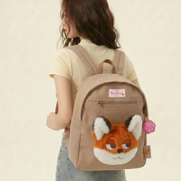 A young woman wearing a light beige herringbone mini backpack featuring a large 3D plush Nick Wilde fox face and a pink paw print charm.